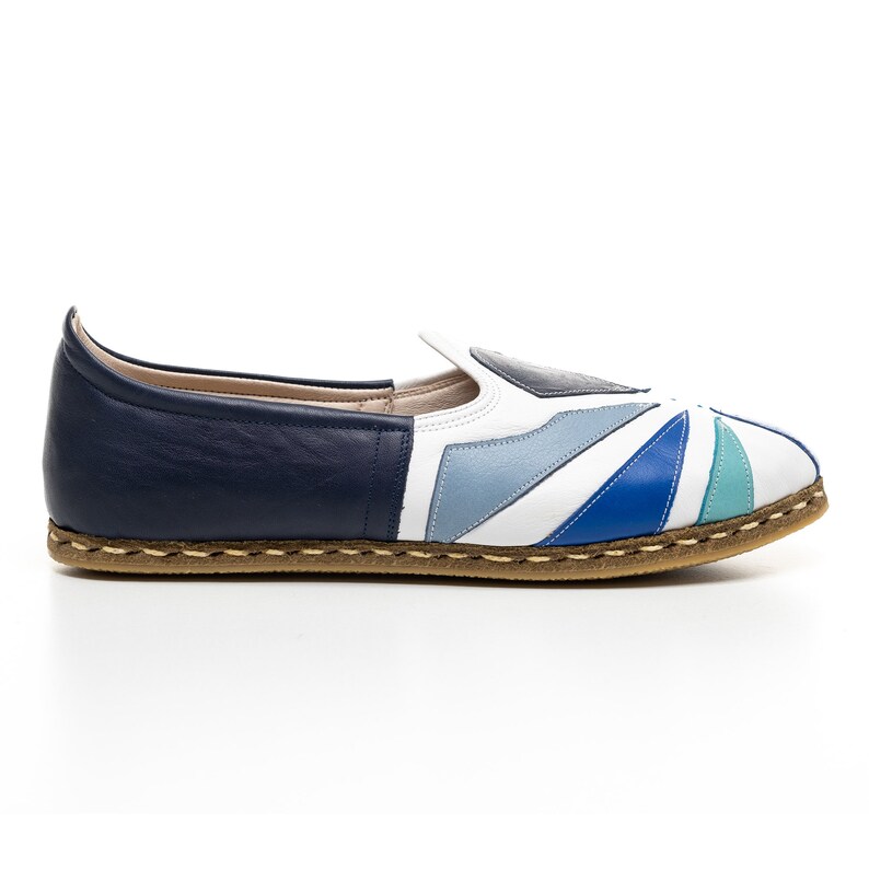 May include: A pair of white leather slip-on shoes with a blue, teal, and gray geometric pattern. The shoes have a brown leather sole.