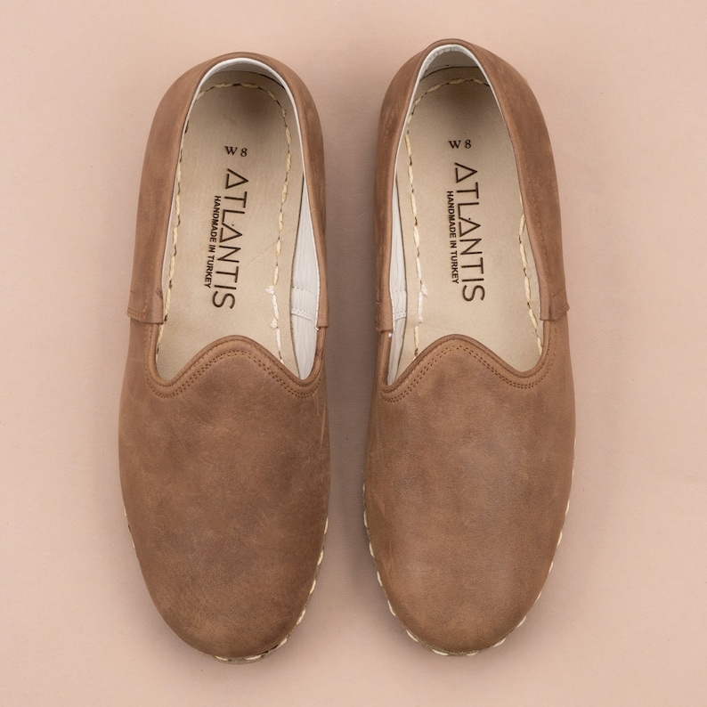 Puede incluir: Un par de zapatos marrones de cuero con un borde cosido. Los zapatos tienen una etiqueta blanca en el interior que dice "ATLANTIS HANDMADE IN TURKEY W 8".