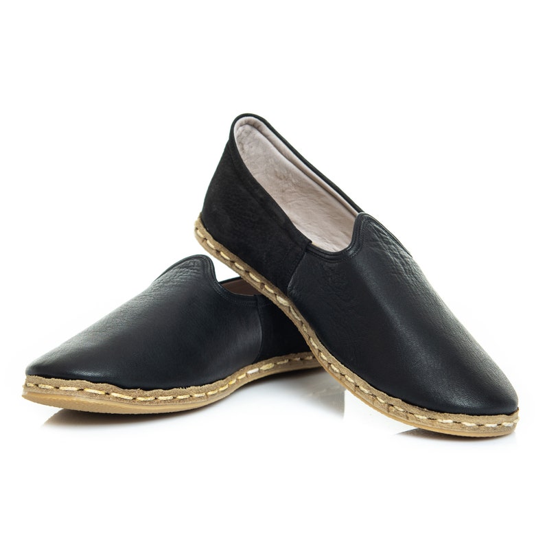 May include: A pair of black leather slippers with a brown stitched trim. The slippers have a soft, comfortable lining.