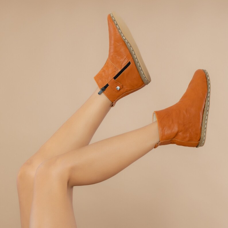 May include: A pair of brown leather ankle boots with a zipper on the side. The boots are worn by a person with their legs raised in the air.