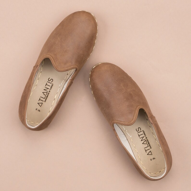 Puede incluir: Un par de zapatos marrones de cuero con suela blanca. Los zapatos tienen una etiqueta en el interior que dice "ATLANTIS Hecho a mano en Turqu&iacute;a".