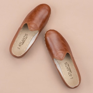 May include: A pair of brown leather slippers with a white sole and the text "ATLANTIS HANDMADE IN TURKEY" on the inside.