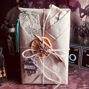 May include: A brown paper package tied with twine and decorated with a dried orange slice, star anise, and cinnamon stick. The package has a silver tag with the word "Cherish" on it.