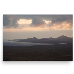 Può includere: Una vista panoramica di un paesaggio vulcanico con un'estensione d'acqua in primo piano. Il cielo è nuvoloso con un tocco di rosa nelle nuvole.