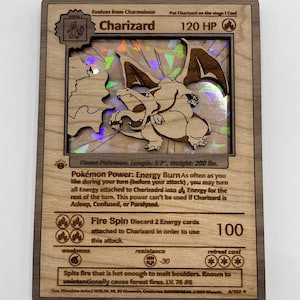 May include: A wooden Pokemon card featuring Charizard, a fire-type Pokemon. The card has a holographic image of Charizard with a red, orange, and yellow color scheme. The card text reads "Charizard, 120 HP, Fire Spin: Discard 2 Energy cards attached to Charizard in order to use this attack.  Spits fire that is hot enough to melt boulders. Known to unintentionally cause forest fires. LV. 76 86".