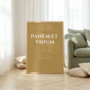 Puede incluir: Un cuadro rectangular con marco y fondo de color amarillo mostaza. El texto en blanco dice PANEM ET VINUM seguido del texto más pequeño that's... basically a balanced diet. El marco es de madera clara con un perfil sencillo y limpio.