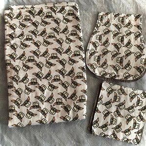 Puede incluir: Tres baberos de beb&eacute; de tela blanca con un patr&oacute;n repetido de un beb&eacute; de dibujos animados con ojos grandes y boca abierta. Los baberos son de diferentes tama&ntilde;os y formas.