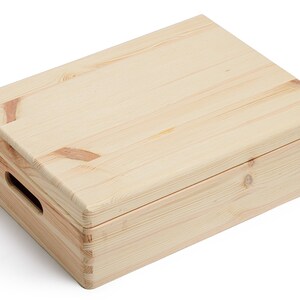 May include: A rectangular wooden box with a lid, constructed from light-colored pine. The box features a handle cutout on one side and is assembled with visible dovetail joints. The wood grain is prominent, and the box appears to be unfinished.
