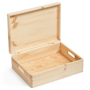 May include: An open, light-colored wooden box with a hinged lid. The box has a rectangular shape with cut-out handles on the sides. The lid is partially open, revealing the interior. The wood grain is visible throughout the box.