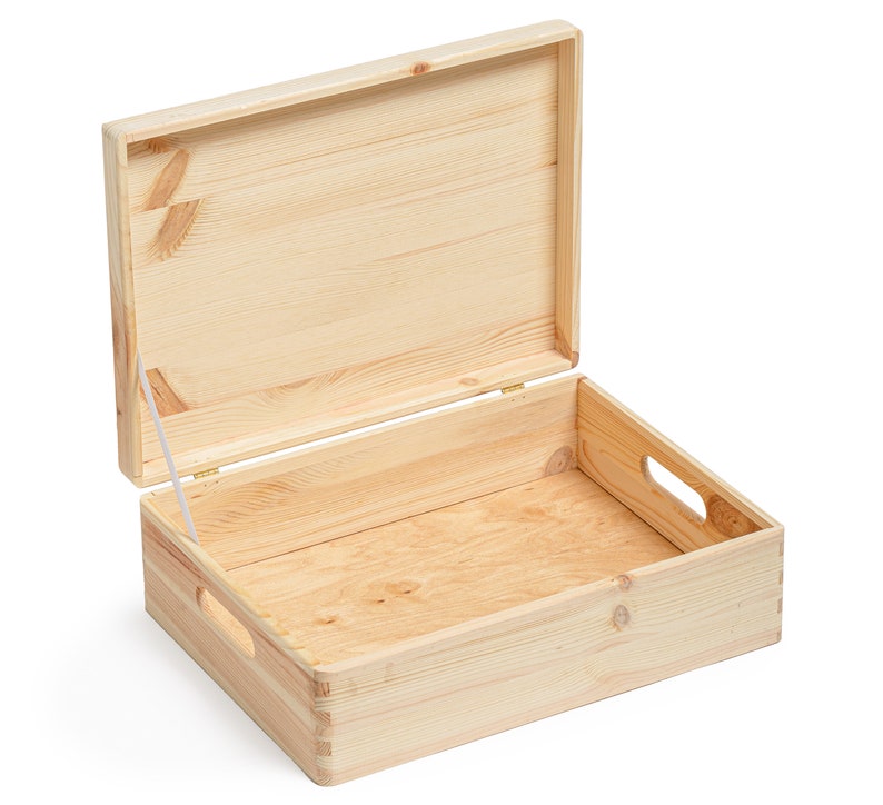 May include: An open, light-colored wooden box with a hinged lid. The box has a rectangular shape with cut-out handles on the sides. The lid is partially open, revealing the interior. The wood grain is visible throughout the box.