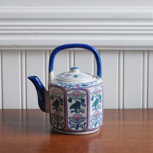 May include: A blue and white teapot with a floral design. The teapot has a hexagonal body and a blue handle.