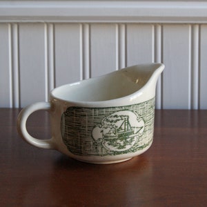 May include: White ceramic gravy boat with a green design of a ship with smoke stacks. The design is on a white background with a green border.