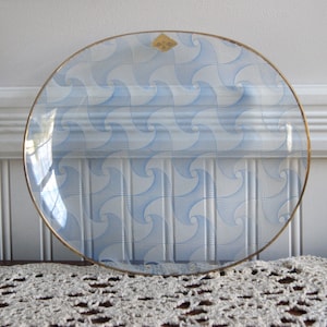 May include: A clear glass oval serving dish with a gold rim and a blue and white geometric pattern. The pattern is made up of repeating swirls.