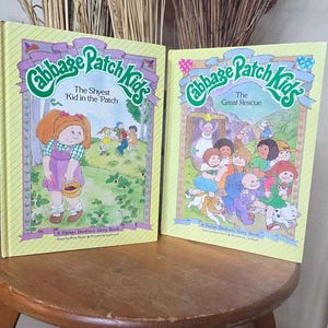 Puede incluir: Dos libros de cuentos amarillos de Cabbage Patch Kids titulados The Shyest Kid in the Patch y The Great Rescue, publicados por Parker Brothers. Debajo hay un libro titulado American Heritage con una ilustración de un caballo y un jinete.