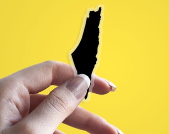 May include: A black sticker in the shape of a country's outline, held against a yellow background. The sticker has a white border. The sticker is being held by a person.