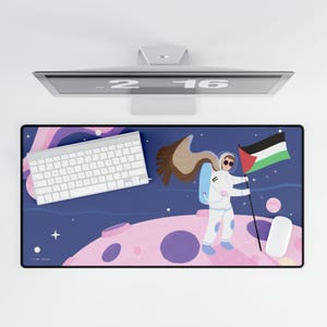 Könnte beinhalten: Rechteckiges Mauspad mit Weltraum-Design. Es zeigt einen Cartoon-Astronauten, der eine Flagge mit den Farben Schwarz, Weiß, Grün und Rot hält. Eine weiße Tastatur und Maus sind ebenfalls sichtbar. Der Hintergrund ist dunkelblau mit rosa Planeten.