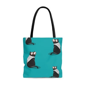 May include: A teal tote bag with black handles featuring a repeating pattern of black cats wearing round orange-rimmed sunglasses and white and black checkered scarves. The cats are depicted in a seated position against the solid teal background.