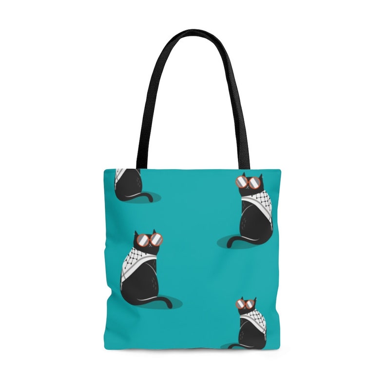 May include: A teal tote bag with black handles featuring a repeating pattern of black cats wearing round orange-rimmed sunglasses and white and black checkered scarves. The cats are depicted in a seated position against the solid teal background.
