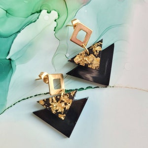 May include: A pair of black triangle earrings with gold accents. Each earring features two layered triangles with gold leaf accents and a gold square charm.