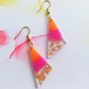 May include: A pair of triangle-shaped earrings with pink and orange resin and gold flakes. The earrings have gold hooks.
