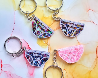 May include: Four keychains featuring glitter-filled resin charms shaped like underwear with the text "Positive Pants" on each. The charms are attached to silver key rings.