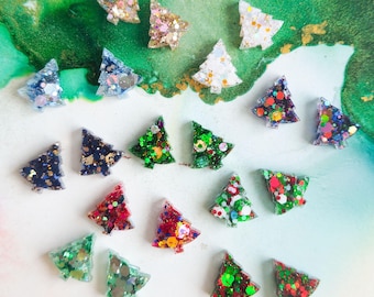 May include: A collection of small, triangular Christmas tree-shaped ornaments made of resin. Each piece features a unique combination of embedded colorful glitter, sequins, and metallic flakes in various shades of red, green, blue, gold, and white.