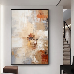 以下が含まれることがあります： 茶色、白、グレーの配色を使用した抽象画。絵画は黒い額縁に入っていて、白い壁にかけられています。