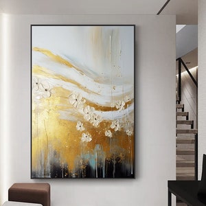 May include: Abstract painting with white flowers on a gold and black background. The painting is framed in black and hangs on a white wall.