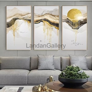 May include: A set of three abstract landscape paintings with gold accents. The paintings feature a mountain range with a golden sun in the background. The paintings are framed in gold.