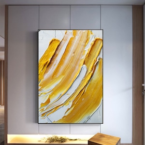 May include: Abstract painting with thick strokes of yellow and white paint on a canvas. The painting is framed in black.