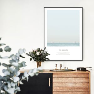 Puede incluir: Una impresi&oacute;n enmarcada de un paisaje mar&iacute;timo con un velero en la distancia. El texto "THE SEASCAPE" est&aacute; impreso debajo de la imagen. La impresi&oacute;n est&aacute; colgada en una pared blanca sobre una c&oacute;moda de madera.