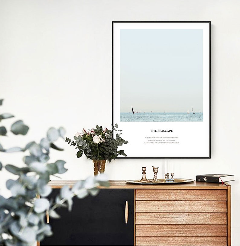 Puede incluir: Una impresi&oacute;n enmarcada de un paisaje mar&iacute;timo con un velero en la distancia. El texto "THE SEASCAPE" est&aacute; impreso debajo de la imagen. La impresi&oacute;n est&aacute; colgada en una pared blanca sobre una c&oacute;moda de madera.