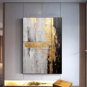 May include: Abstract painting with gold and black accents on a white background. The painting has a textured surface and is framed in a black frame.