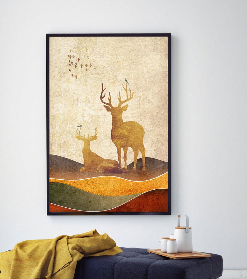 May include: A framed print with a vintage aesthetic featuring two golden deer silhouettes against a textured background of brown, green, and yellow hills. Small blue birds are perched on the deer's antlers and flying in a circle above them.