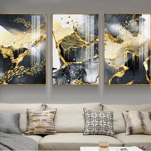May include: Three abstract art prints with gold leaf accents. The prints feature a black and white background with gold lines and shapes. The prints are framed in gold.