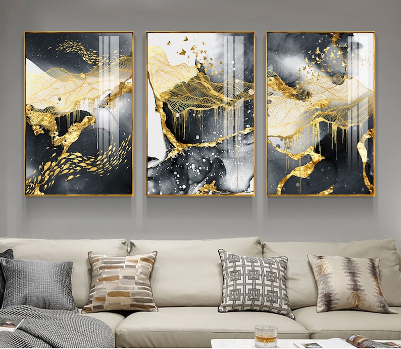 May include: Three abstract art prints with gold leaf accents. The prints feature a black and white background with gold lines and shapes. The prints are framed in gold.