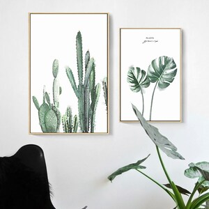 May include: Two framed prints with botanical illustrations. The first print features a group of cacti in shades of green. The second print features two large monstera leaves in shades of green. The text "PLANTS" is written in black at the top of the second print.
