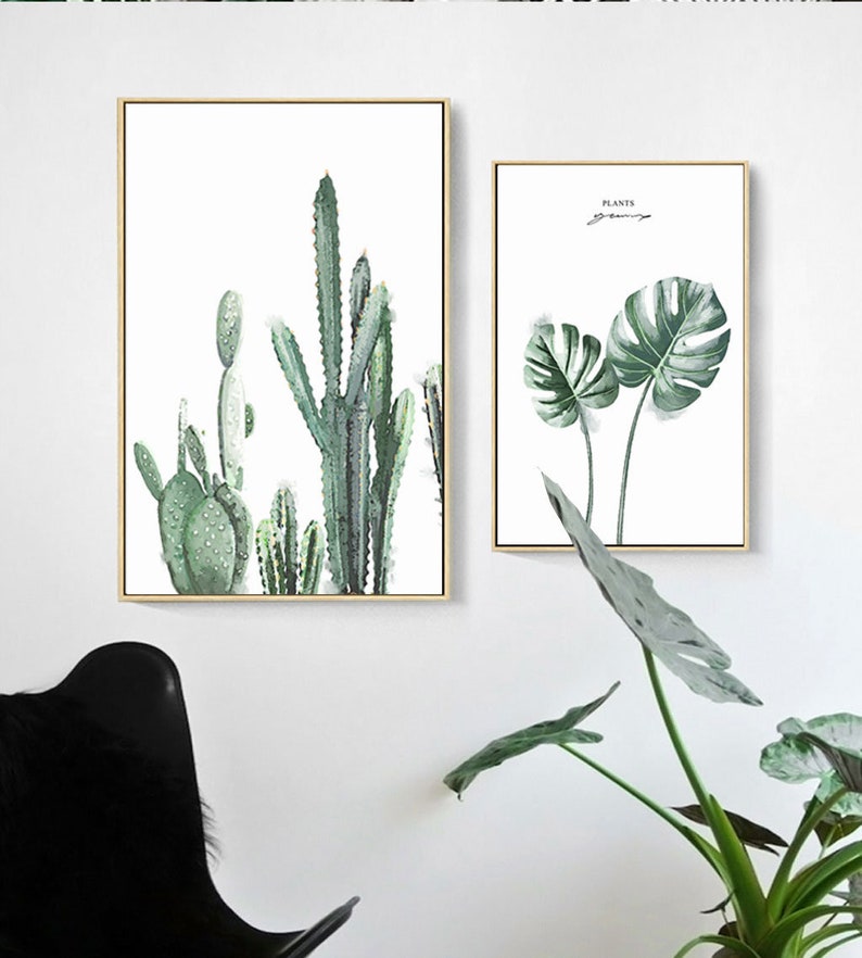 May include: Two framed prints with botanical illustrations. The first print features a group of cacti in shades of green. The second print features two large monstera leaves in shades of green. The text "PLANTS" is written in black at the top of the second print.