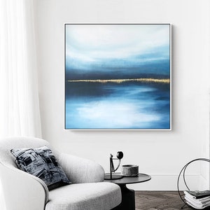Puede incluir: Pintura abstracta de paisaje con un esquema de color azul y dorado. La pintura representa un horizonte con una masa de agua y un cielo con nubes. La pintura está enmarcada en un marco blanco.