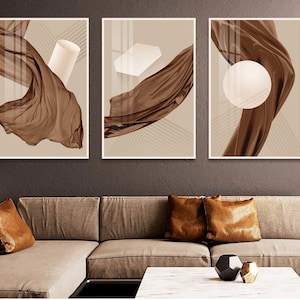 May include: Three abstract art prints with brown fabric draped over geometric shapes. The prints have a beige background with brown lines.