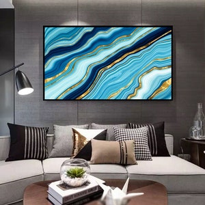 May include: Abstract wall art print featuring a blue and gold marble design. The print has a black frame and is hanging on a gray wall above a couch.