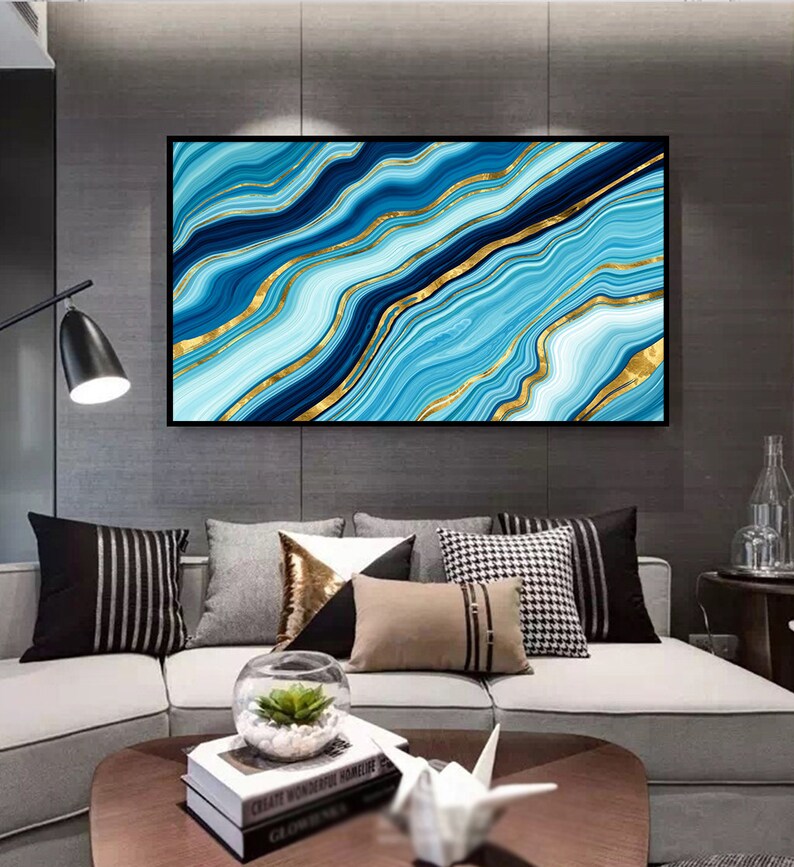 May include: Abstract wall art print featuring a blue and gold marble design. The print has a black frame and is hanging on a gray wall above a couch.