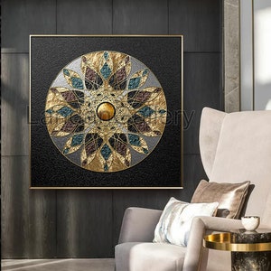 Puede incluir: Una impresión en lienzo cuadrada con un diseño de mandala dorado, negro y turquesa. El mandala está rodeado de un fondo negro y un marco dorado.