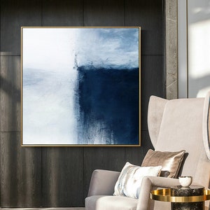 May include: Abstract painting with a white and blue color scheme. The painting is framed in a gold frame and hangs on a dark wood wall.