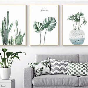 May include: Three framed prints with watercolor illustrations of plants. The first print features a group of cacti in shades of green. The second print features two large monstera leaves in shades of green. The third print features a group of succulents in shades of green in a blue and white pot.