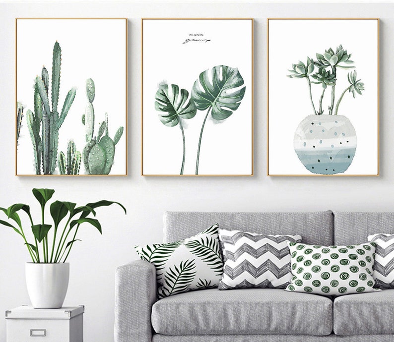 May include: Three framed prints with watercolor illustrations of plants. The first print features a group of cacti in shades of green. The second print features two large monstera leaves in shades of green. The third print features a group of succulents in shades of green in a blue and white pot.