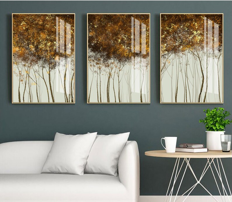 Puede incluir: Tres impresiones art&iacute;sticas enmarcadas que representan una escena de bosque estilizada. La obra de arte tiene una paleta de colores dorados y marrones con una apariencia texturizada. Los &aacute;rboles se representan con troncos finos y oscuros sobre un fondo verde claro. Los marcos son dorados.