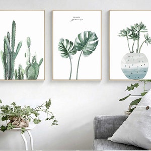 May include: Three framed watercolor paintings of plants. The first painting features a group of cacti in shades of green. The second painting features a large green monstera leaf. The third painting features a succulent plant in a blue and white pot.
