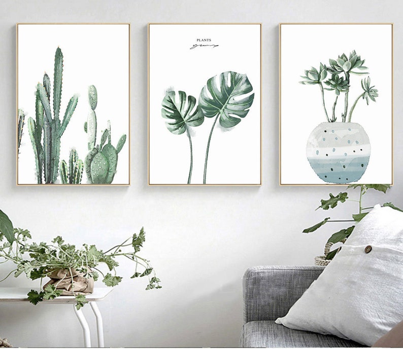 May include: Three framed watercolor paintings of plants. The first painting features a group of cacti in shades of green. The second painting features a large green monstera leaf. The third painting features a succulent plant in a blue and white pot.