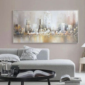 Puede incluir: Una pintura de un paisaje urbano con edificios altos en tonos grises y marrones. Los edificios se reflejan en el agua en primer plano, que es de color dorado claro. El cielo es de color gris claro.